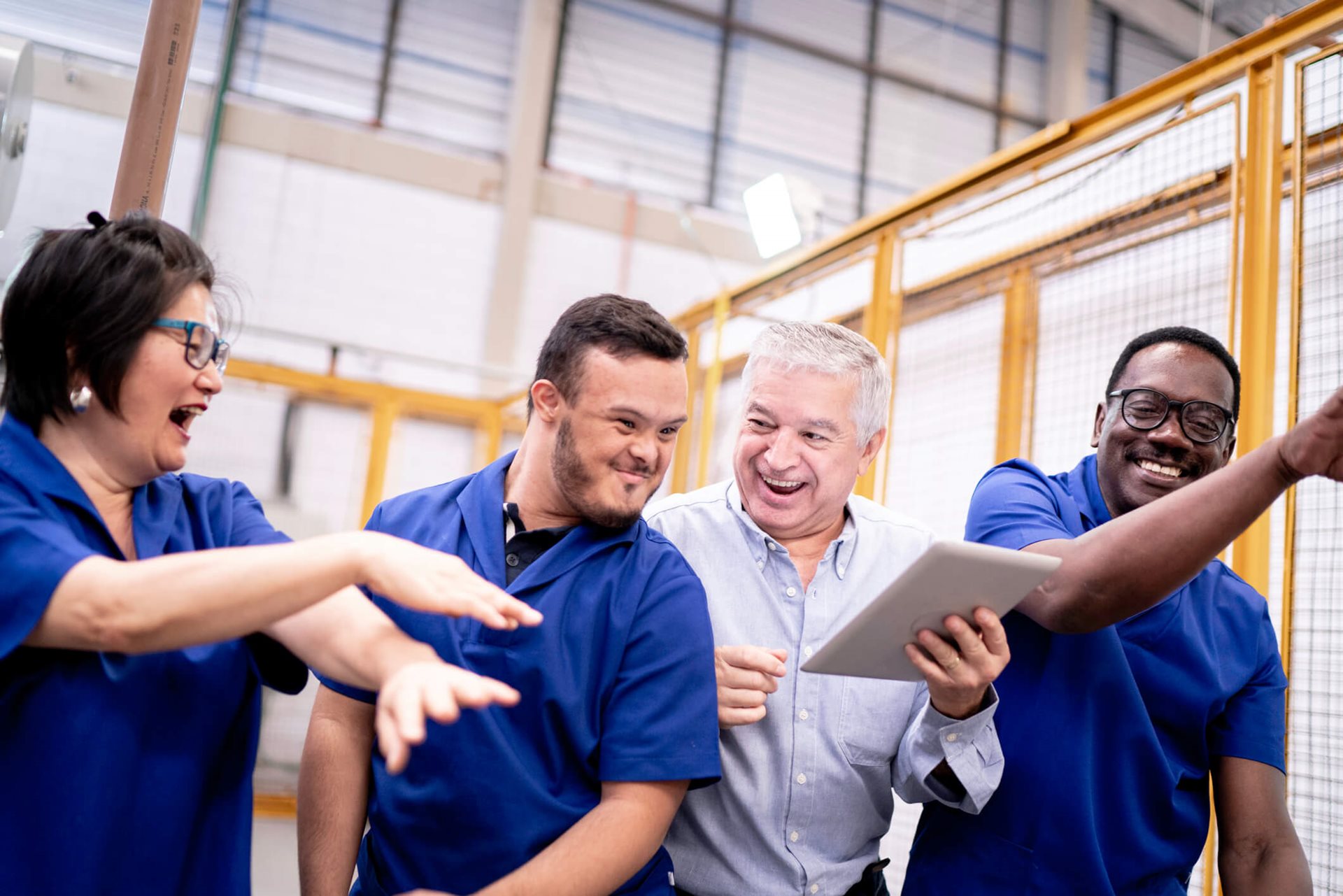 A group of three men and one woman in blue shirts laughing and pointing at an unseen object or event.