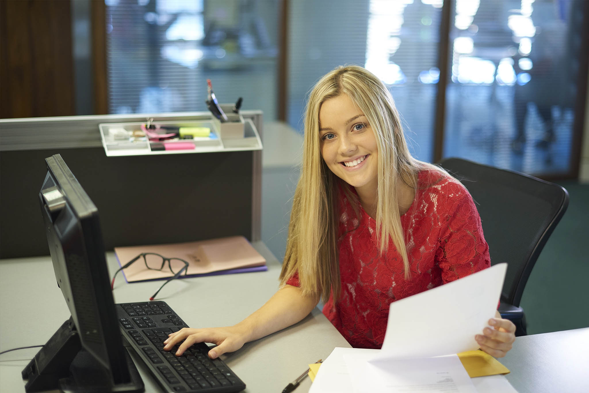 Young interm lady at her desk smiling and looking at the camera.